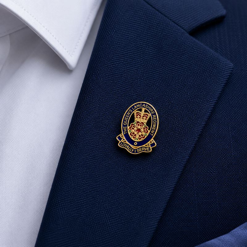 Close-up of a small gold and enamel Queen's Lancashire Regiment lapel badge attached to the lapel of a navy suit jacket.