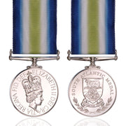 Front and back views of a South Atlantic Medal with a blue, white, and green striped ribbon, displayed on a clean white background with a subtle reflection.
